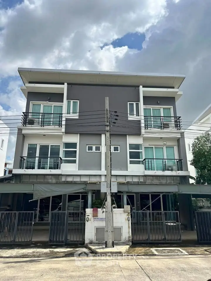 Modern townhouse exterior with sleek design and large windows under a cloudy sky.