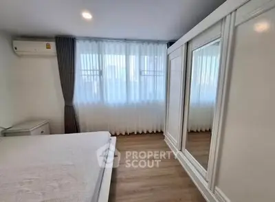 Spacious bedroom with large window and mirrored wardrobe in modern apartment.