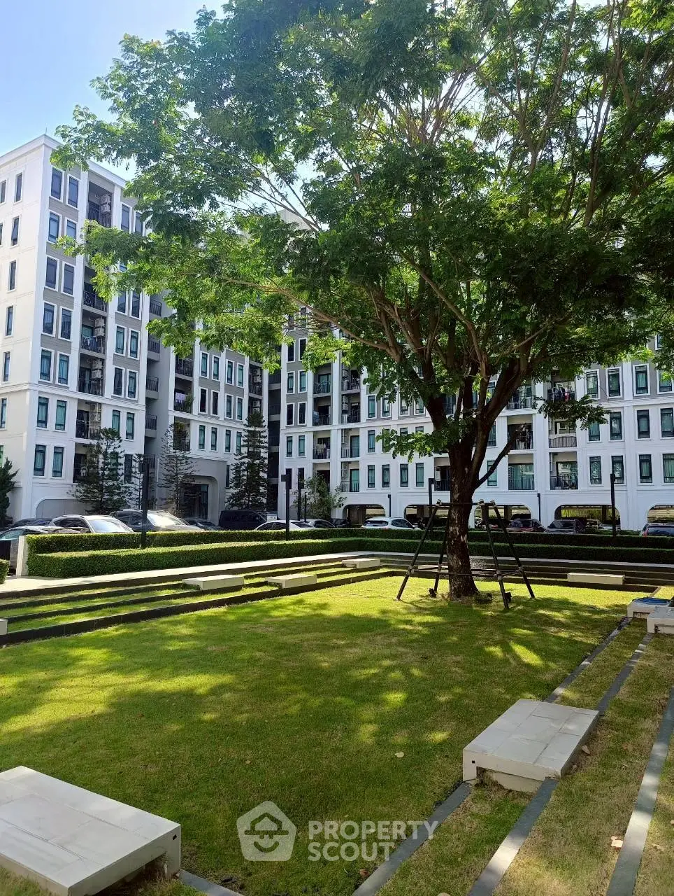 Modern apartment complex with lush green garden and mature tree