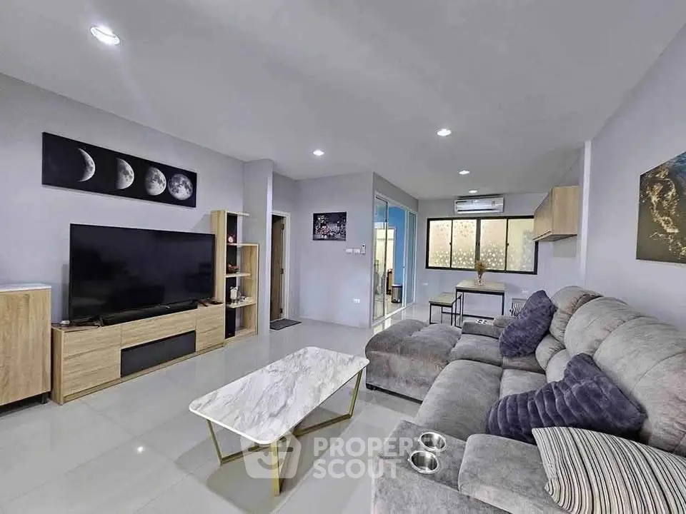 Modern living room with plush gray sofa, large TV, and elegant decor in a spacious open layout.