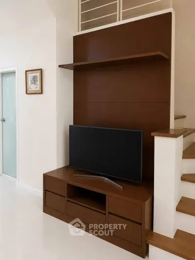 Modern living room with sleek TV stand and staircase, showcasing minimalist design and elegant wood finishes.