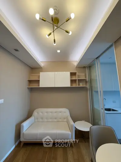 Modern living room with stylish lighting and cozy sofa, adjacent to a sleek kitchen area.
