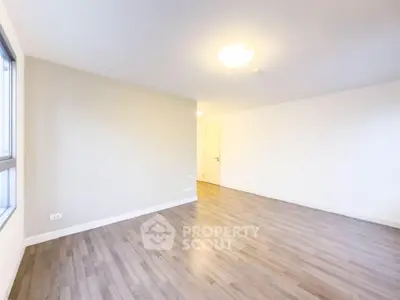 Spacious empty room with wooden flooring and bright lighting, perfect for customization.