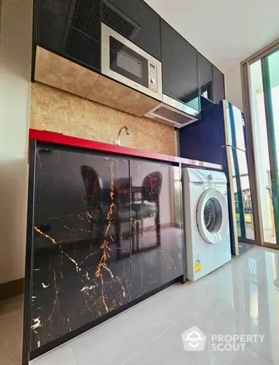 Modern kitchen with sleek black cabinets, built-in microwave, and washing machine