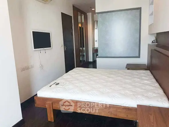 Modern bedroom with wooden bed frame and wall-mounted TV in a minimalist design.