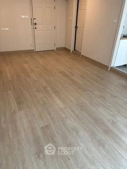 Spacious empty room with wooden flooring and white doors, ideal for customization.