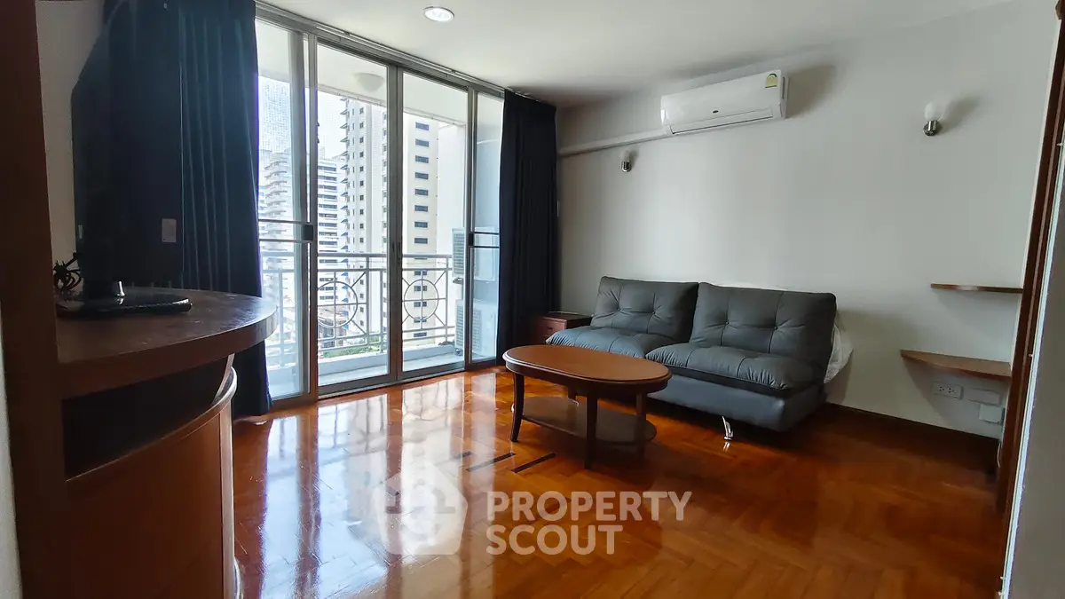 Spacious living room with balcony in modern apartment, featuring polished wooden floors and stylish furniture.