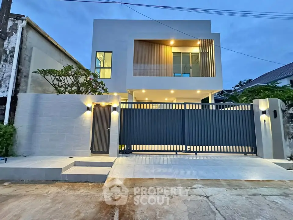 Modern two-story house with sleek design and illuminated facade, featuring a secure gated entrance and contemporary architecture.