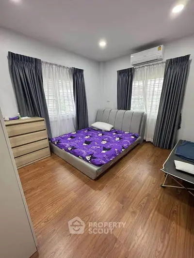 Cozy bedroom with wooden flooring, stylish bed, and ample natural light from large windows.