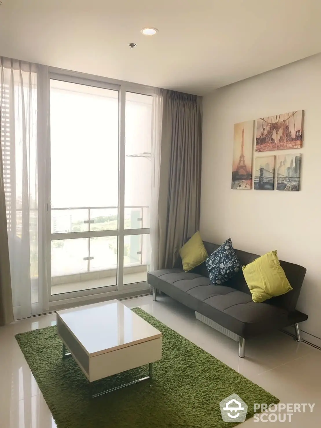 Bright and cozy living room with modern furnishings, large windows allowing ample natural light, and a comfortable grey sofa complemented by a stylish green area rug.