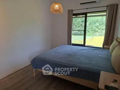 Cozy bedroom with large window offering serene garden view, featuring modern decor and natural light.