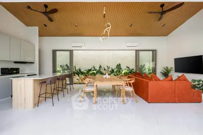 Modern open-plan living room with stylish kitchen and dining area, featuring sleek furniture and lush greenery.