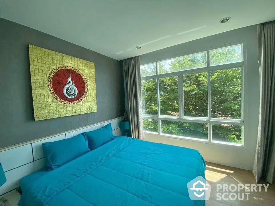 Bright bedroom with large window, blue bedding, and modern decor overlooking lush greenery.