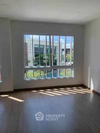 Bright room with large window and wooden flooring, offering a view of modern architecture.