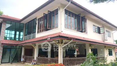 Charming two-story house with large windows and red-tiled roof, surrounded by lush greenery and a cozy porch.