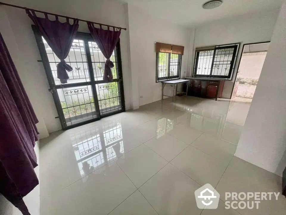 Spacious living room with glossy tiled flooring, large windows with burgundy curtains, and ample natural light, perfect for family gatherings.