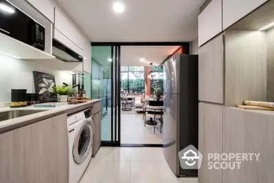 Modern kitchen with sleek cabinetry, washing machine, and open layout leading to a bright living area.