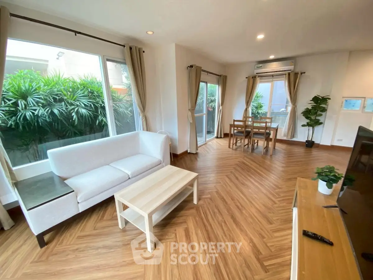Spacious living room with modern decor and large windows overlooking greenery.