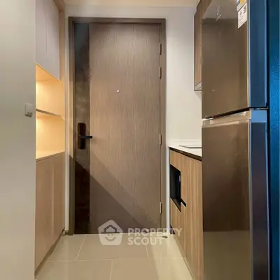 Modern kitchen entrance with sleek wooden cabinetry and stainless steel fridge.