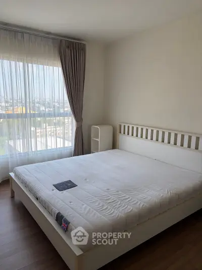 Spacious bedroom with large window offering stunning city views, featuring a modern bed and elegant curtains.