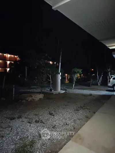 Nighttime exterior view of residential building with parking area and garden.