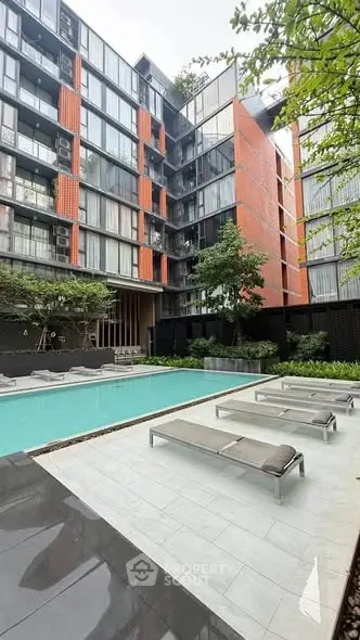 Modern apartment complex with pool and sun loungers, ideal for urban living.