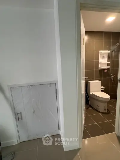 Modern bathroom with sleek design and tiled walls, featuring a compact toilet and shower area.