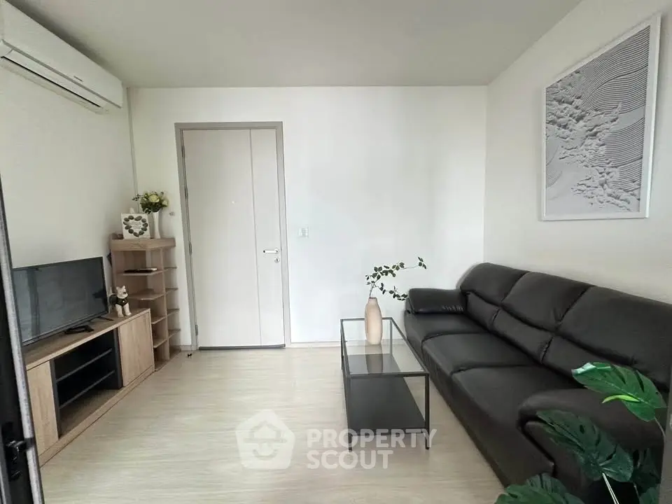 Modern living room with sleek black sofa, minimalist decor, and wall-mounted air conditioner.