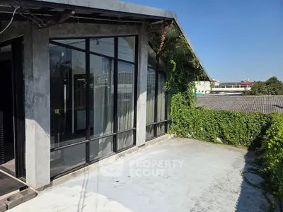 Modern building exterior with large windows and lush greenery on a sunny day.