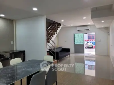 Spacious modern living area with dining table and staircase, featuring sleek design and ample natural light.