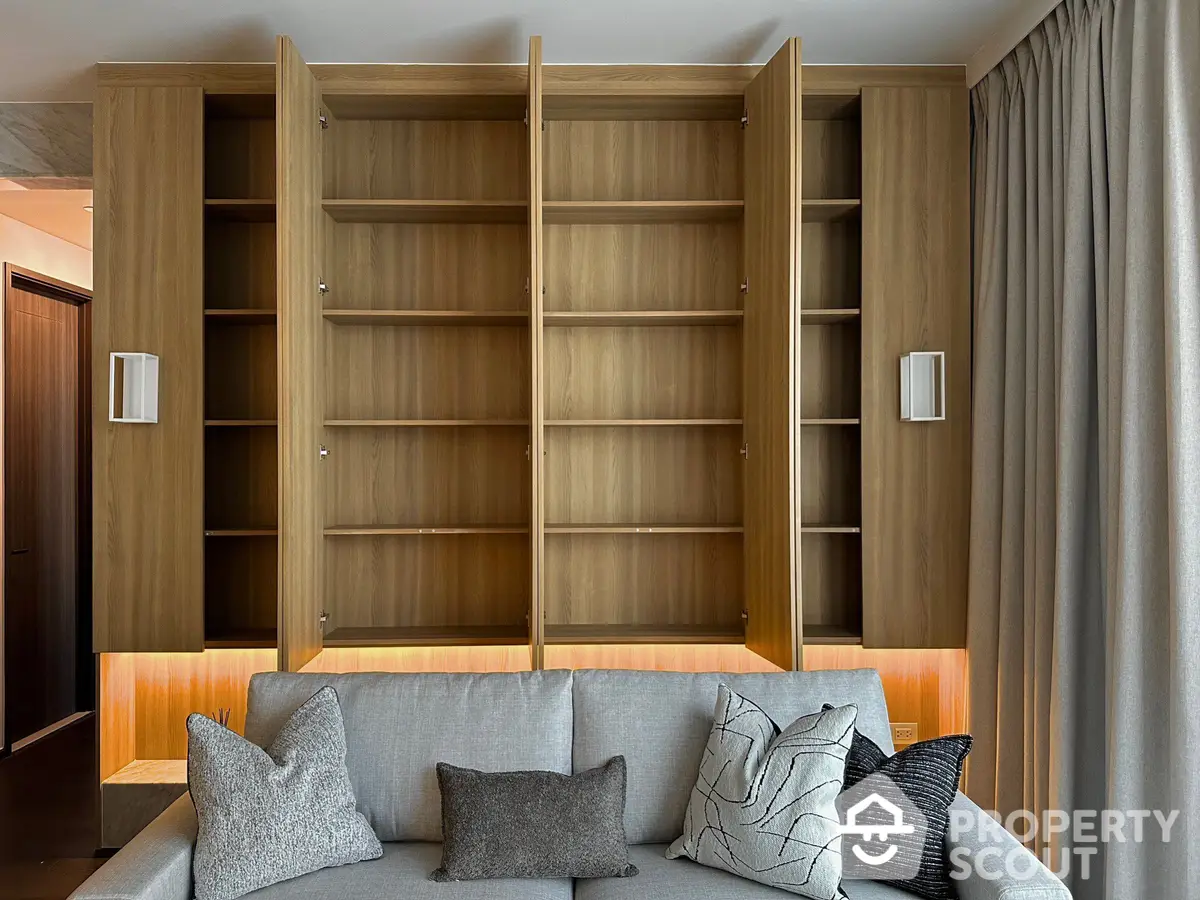 Elegant living room with a large built-in wooden bookshelf and a cozy grey sofa adorned with stylish cushions, creating a sophisticated and inviting atmosphere.