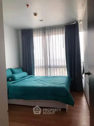 Cozy bedroom with teal bedding and large window offering natural light.