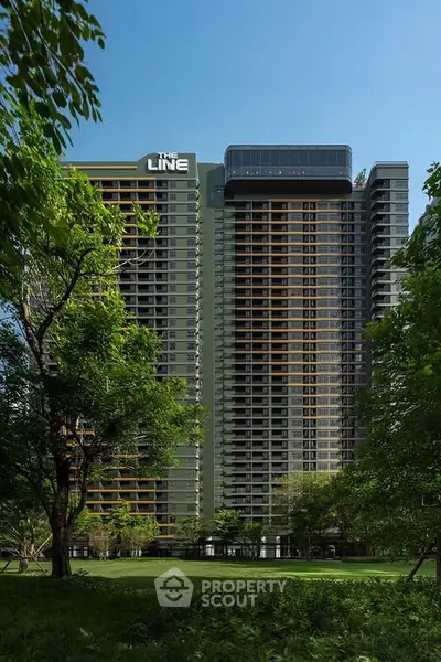 Modern high-rise building with lush green surroundings and clear blue sky.