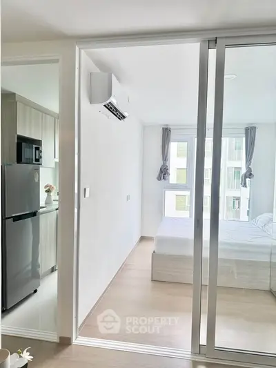 Modern apartment interior with sliding glass doors, featuring a cozy bedroom and a sleek kitchen area.