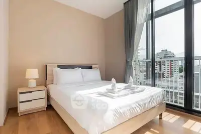 Modern bedroom with large windows and city view, featuring elegant decor and natural light.