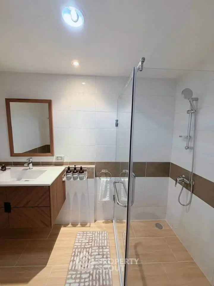 Modern bathroom with glass shower, wooden vanity, and elegant tile flooring.