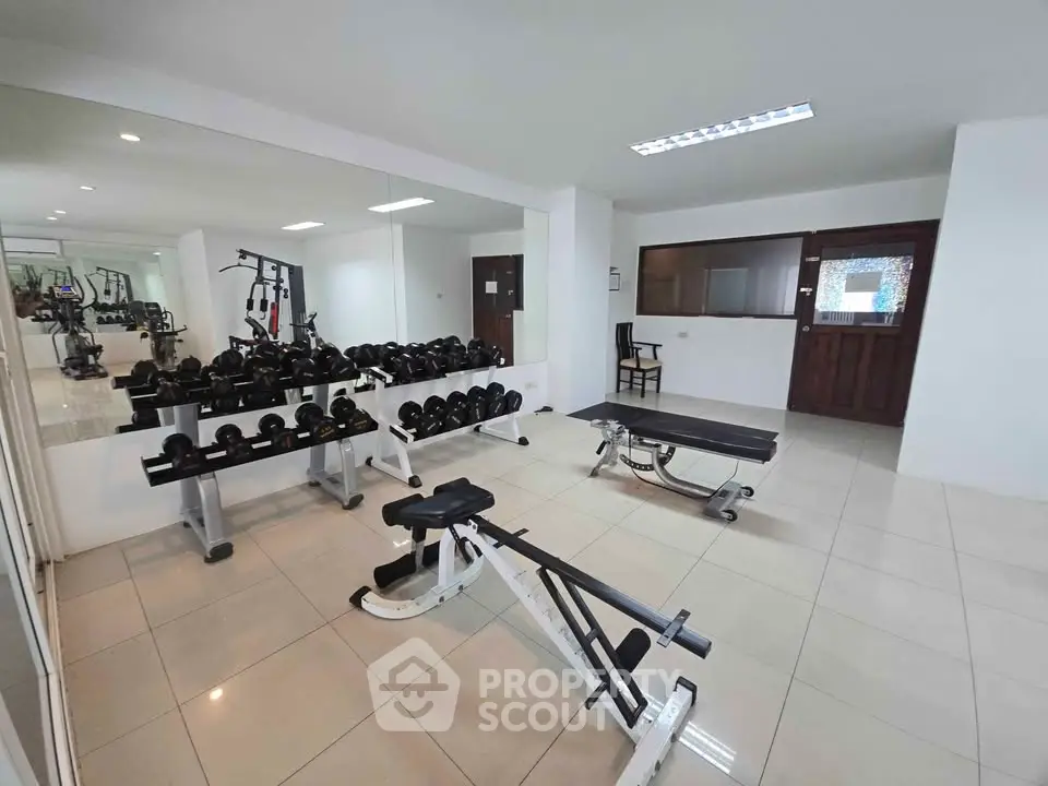 Spacious gym with modern equipment and mirrored walls in a residential building.