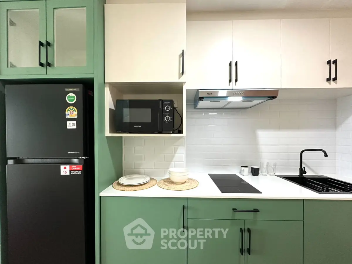 Modern kitchen with green cabinets, black fridge, and sleek appliances in a stylish apartment.