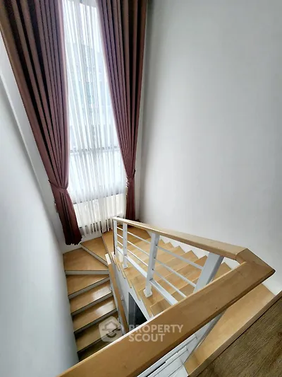 Elegant staircase with wooden steps and modern railing, featuring floor-to-ceiling window with stylish curtains.