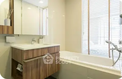 Modern bathroom with sleek wooden vanity and bathtub, featuring natural light through blinds.