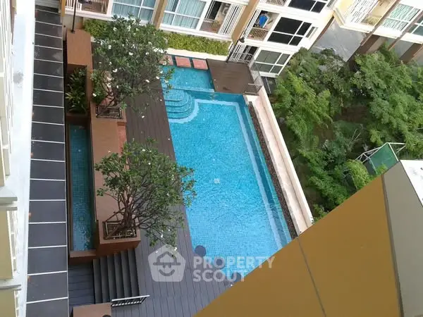 Stunning aerial view of modern apartment pool with lush greenery and stylish deck area.