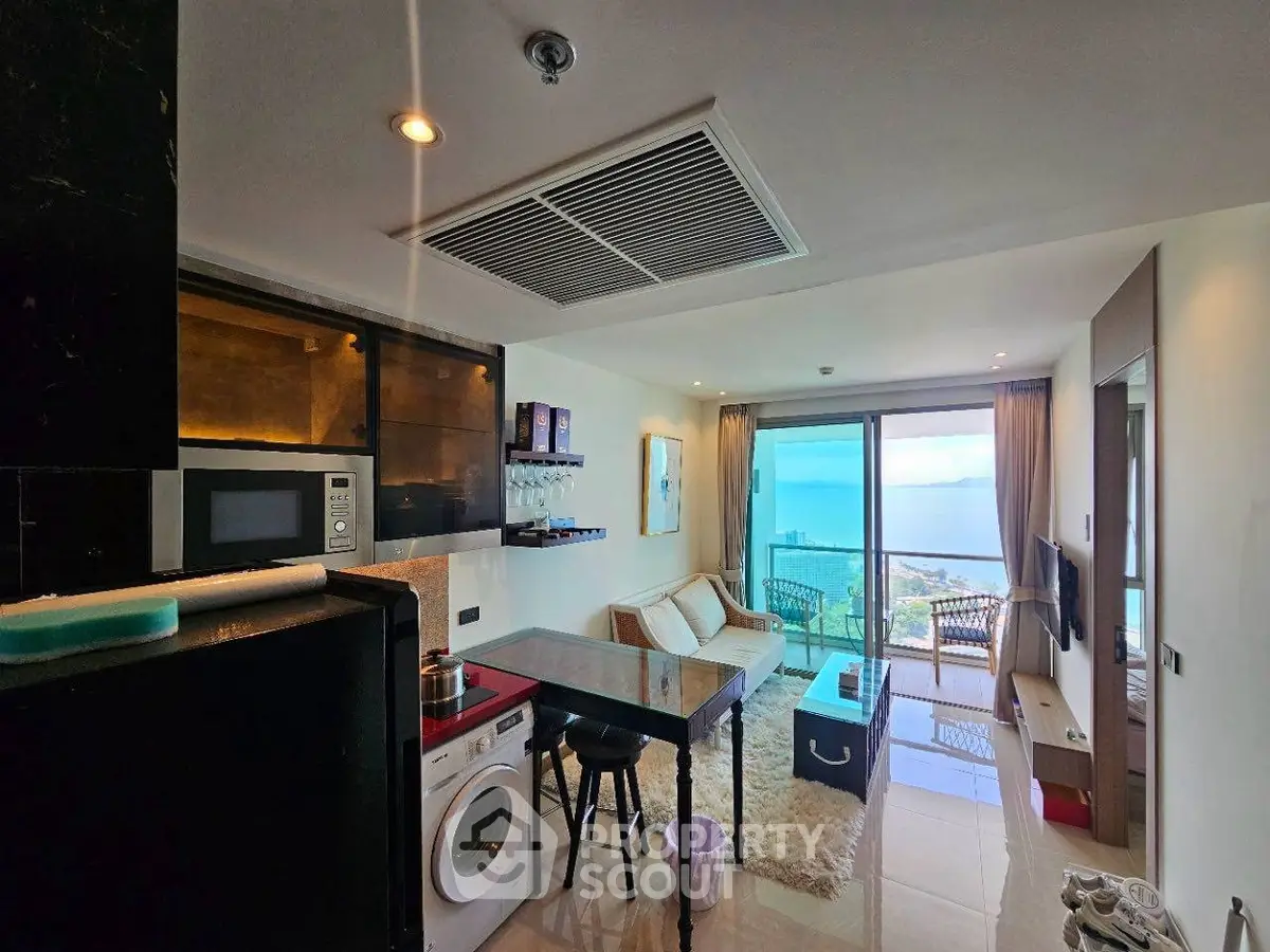 Modern living room with ocean view, open kitchen, and cozy balcony in a high-rise apartment.