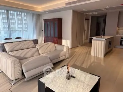 Spacious modern living room with elegant furniture and open kitchen layout, featuring natural light and stylish decor.