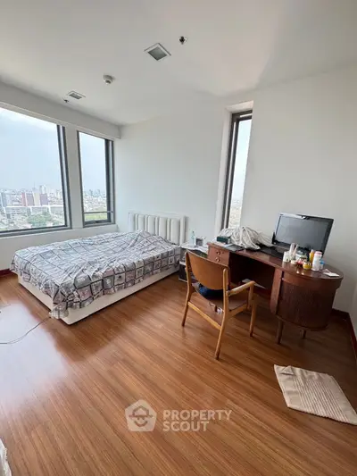 Spacious bedroom with city view, featuring a cozy bed and wooden desk, perfect for urban living.