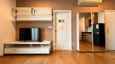 Modern living room with sleek TV unit and mirrored wardrobe, adjacent to a stylish kitchen with built-in appliances.