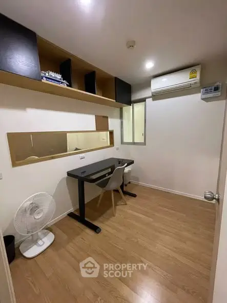 Modern study room with wooden flooring, sleek desk, and wall-mounted shelves in a cozy apartment.