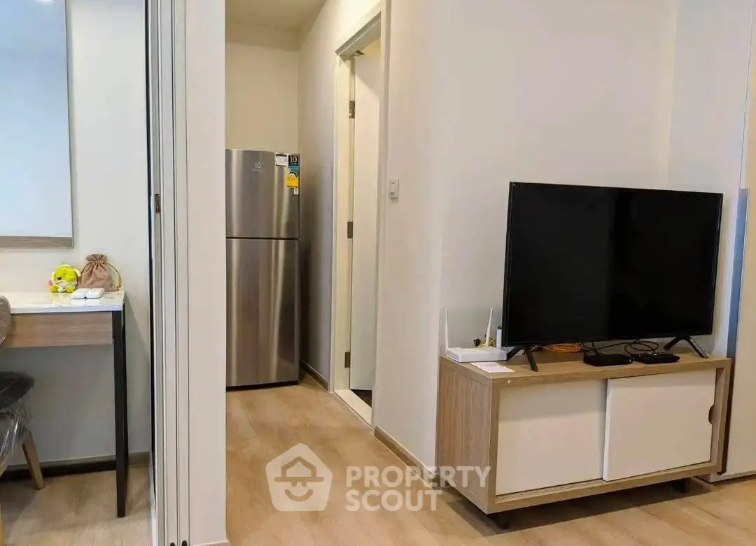 Modern living room with sleek TV setup and stainless steel fridge in cozy apartment.