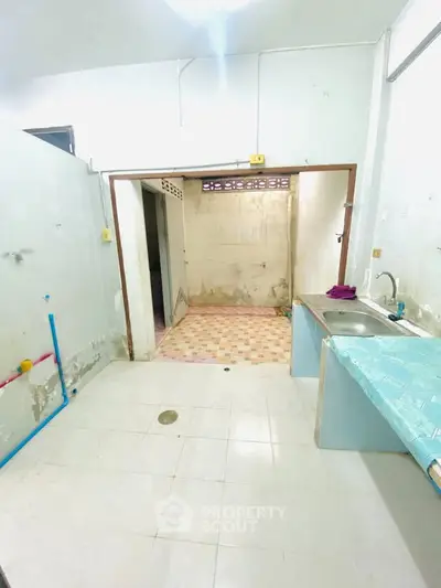 Spacious kitchen area with tiled flooring and stainless steel sink, ready for renovation.