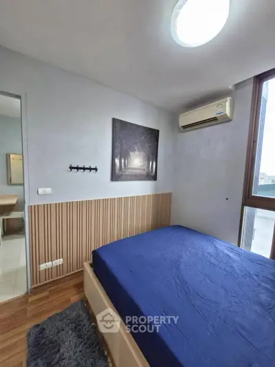 Cozy bedroom with blue bedding, wooden accents, and large window for natural light.