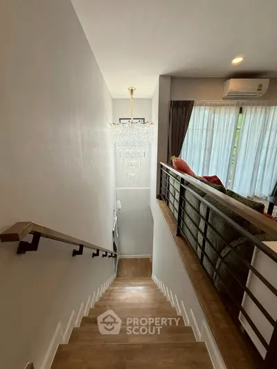 Elegant staircase with chandelier leading to a cozy living room with modern decor.
